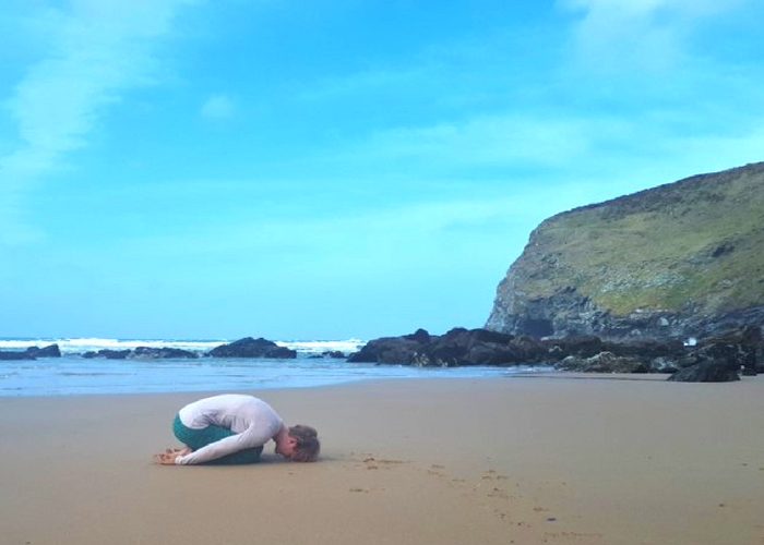 childs pose on the beach in cornwall cliffs and sea
