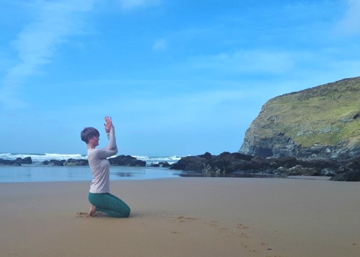 seated eagle yoga pose on beach cliffs and waves cornwall