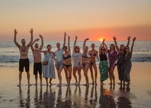 group of people on beach with hands in air at sunset